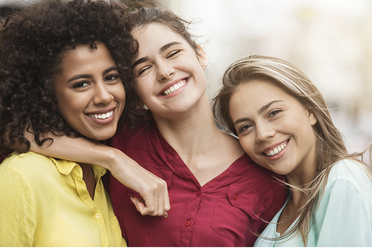 three young women smiling with their arms around each other.